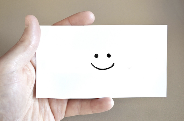 decorative image of a hand holding a card with happy face drawn on the card.